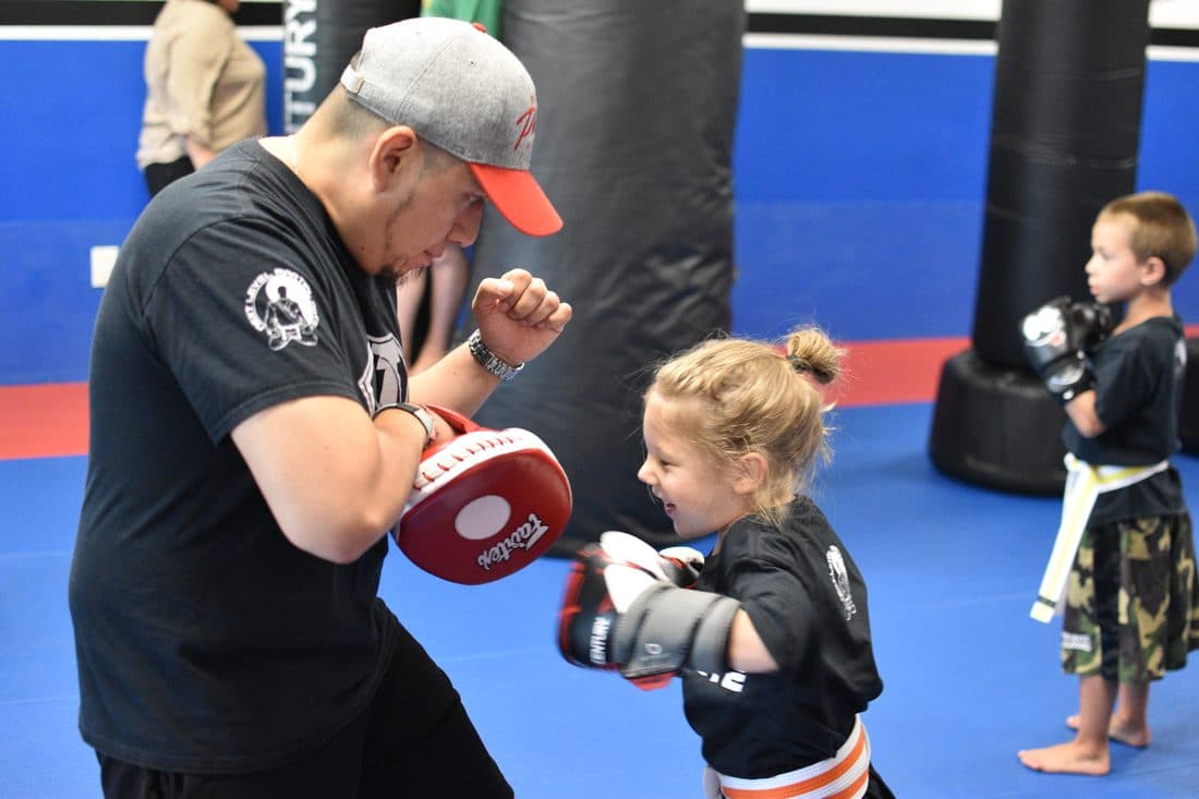 Coach holding focus mitts for a young student in the Little Ninjas kids class