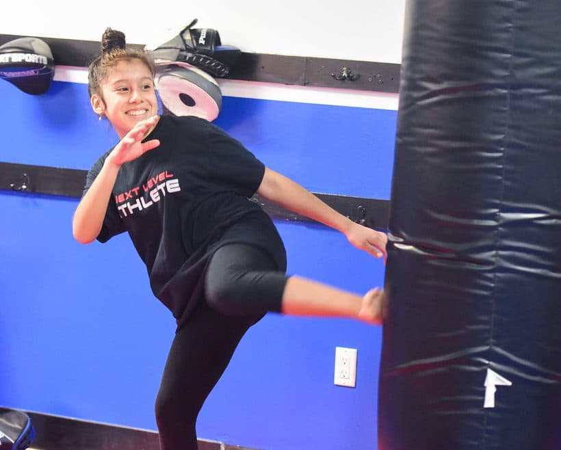 Smiling teen in a Next Level Athlete shirt landing a kick during a Muay Thai class at Next Level Martial Arts