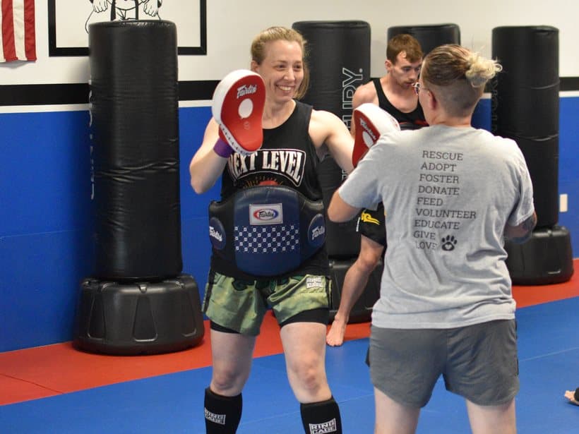 Smiling adult member holding Thai pads during an advanced Muay Thai class at Next Level